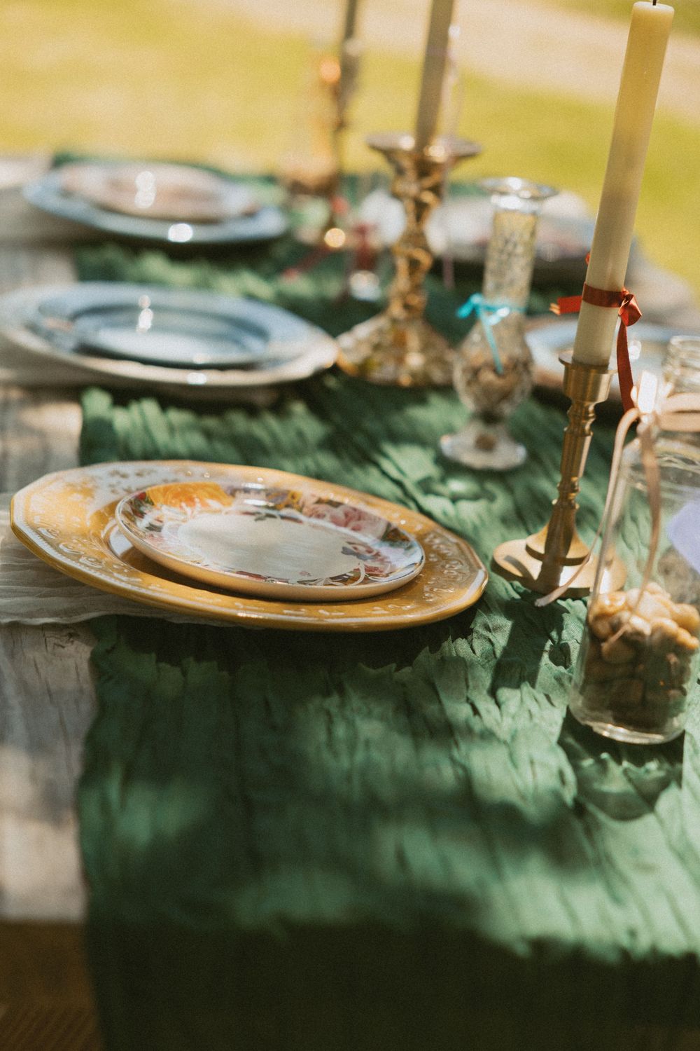 Elegant table setting with emerald green linens, gold charger plates, and candlesticks in soft natural lighting.