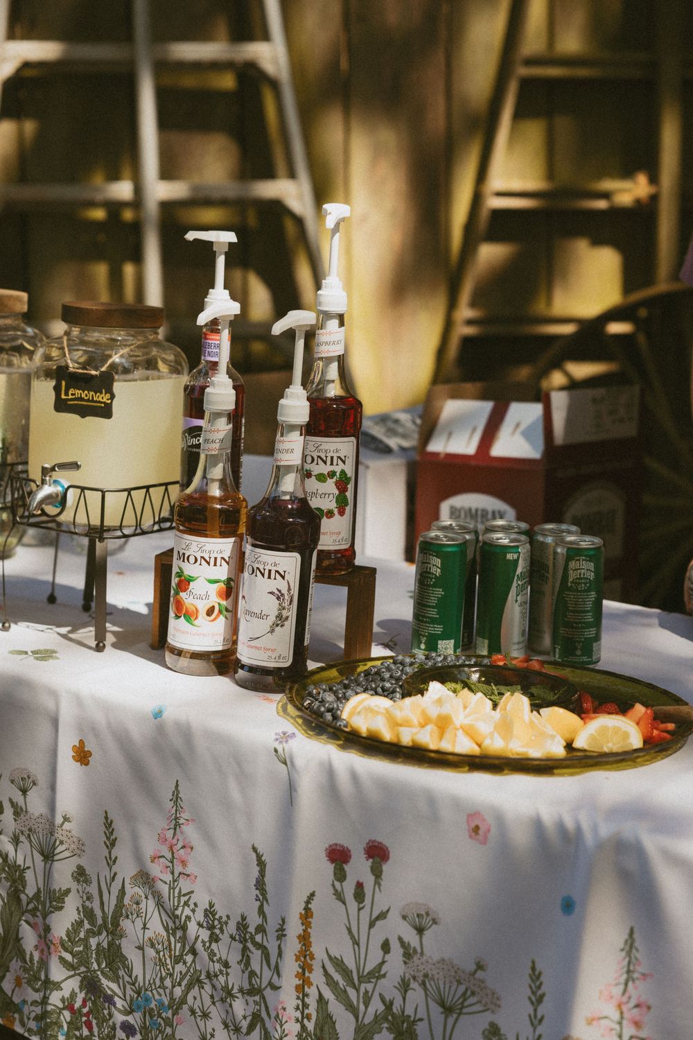A bar setup with various liquor bottles and mixers displayed on a white tablecloth with decorative floral arrangements.