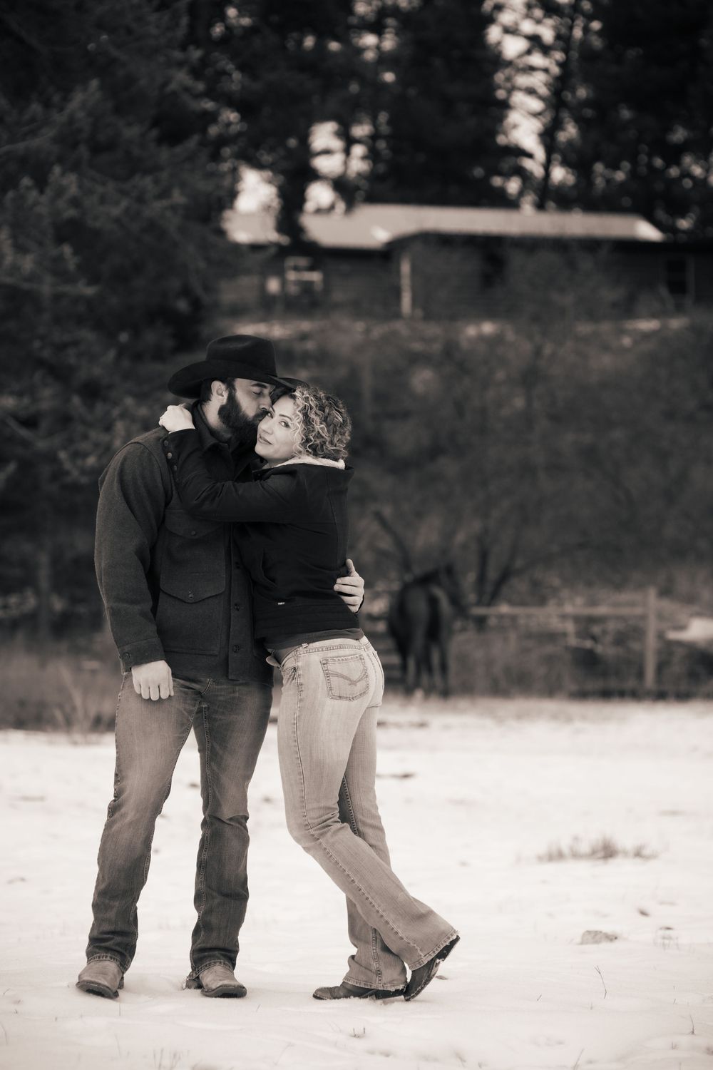 A couple embracing in a tender moment on a snowy winter day with trees in the background.