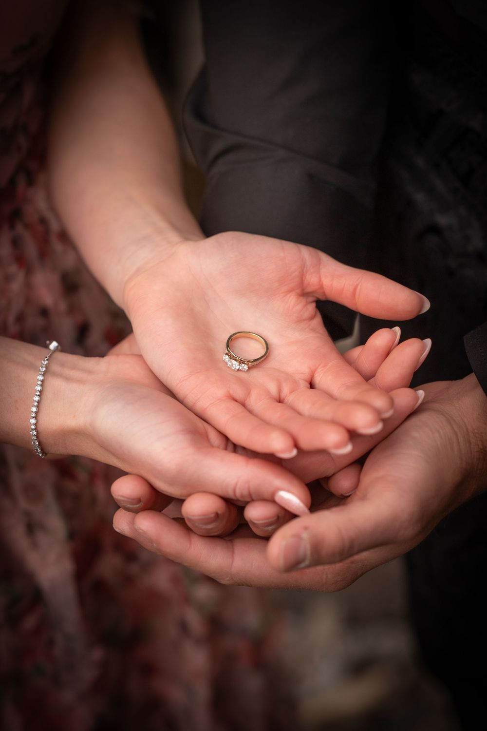 A sequence of hands holding and revealing a delicate gold engagement ring in soft lighting.