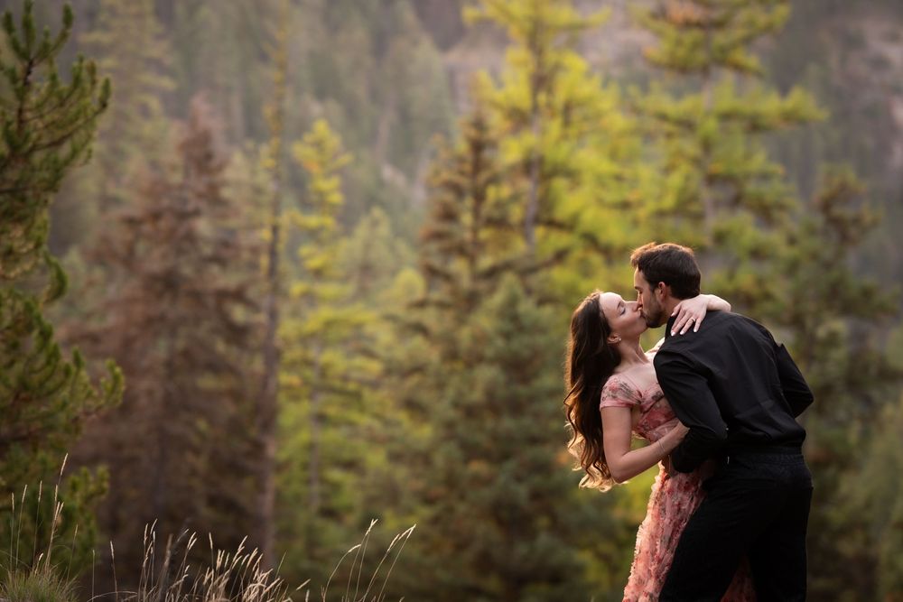 A couple shares tender moments against a backdrop of evergreen forest.