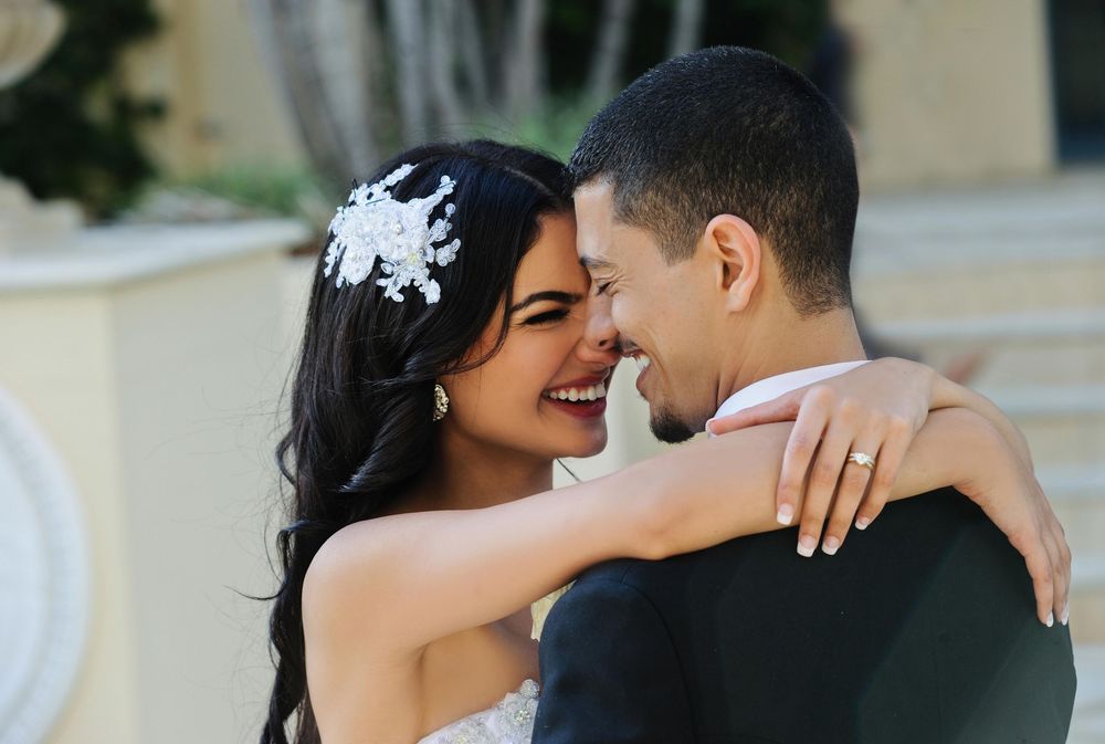 Joyful bride in lace gown embracing groom outdoors, smiling radiantly on their wedding day.