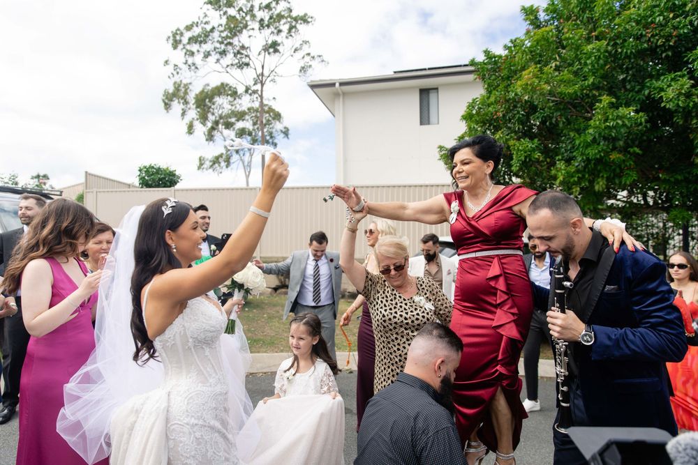 Bride in white gown dances joyfully outdoors with guests at wedding celebration.
