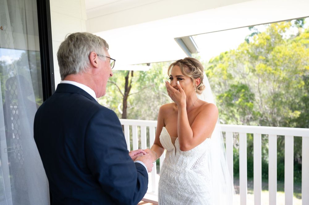 Emotional bride wiping tears during heartfelt first look moment with father on wedding day.