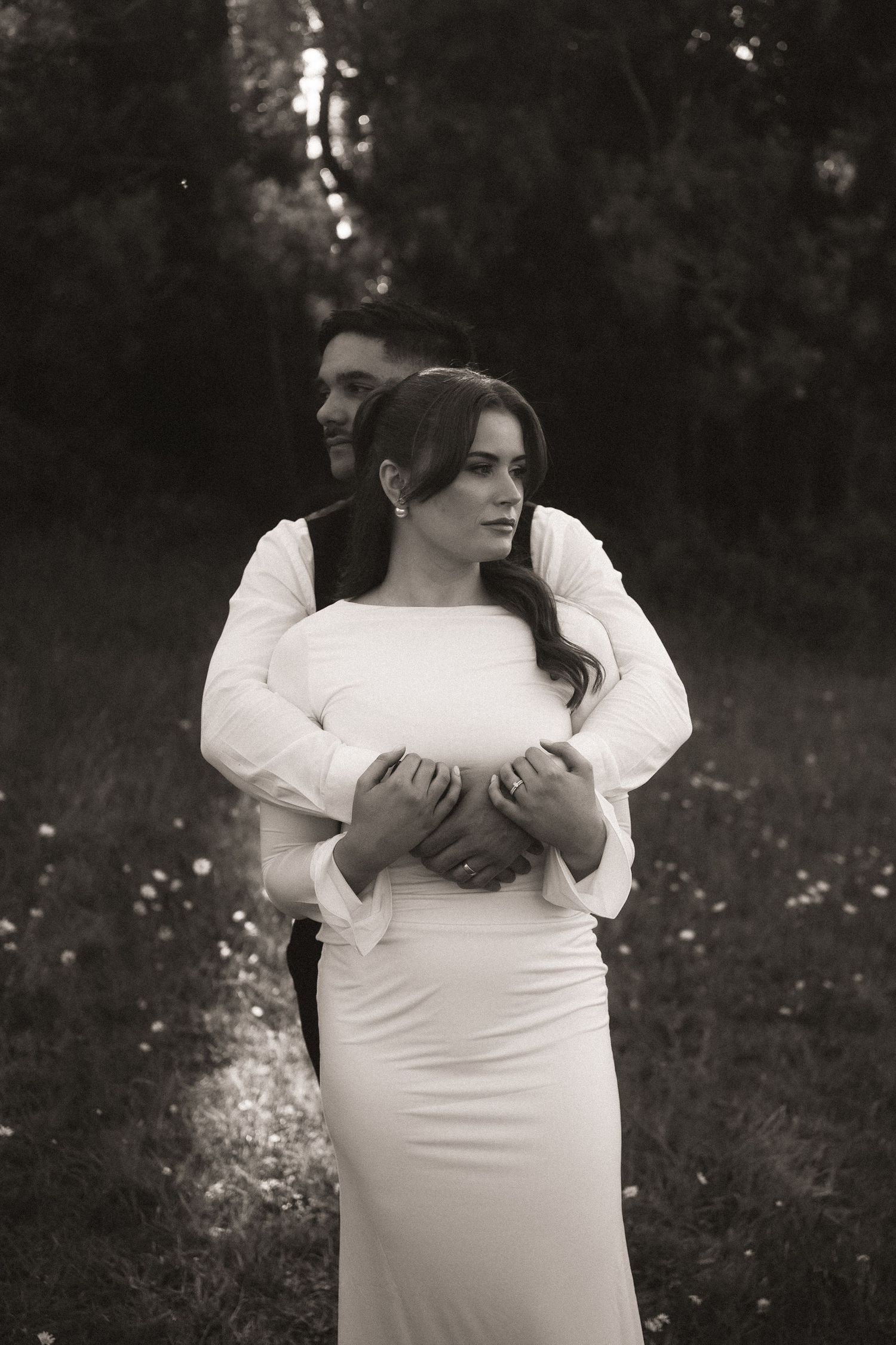 A series of black and white portraits showing someone in a white dress embracing themselves in a field of flowers.
