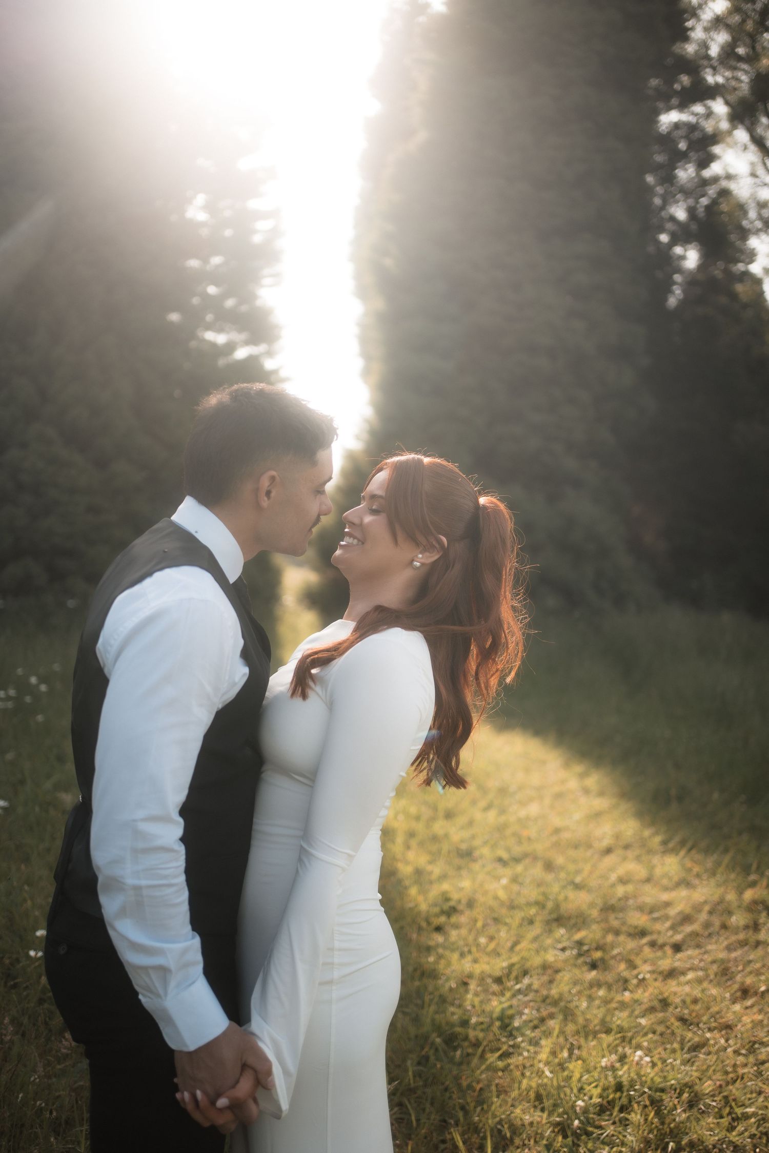 A romantic couple in wedding attire share an intimate moment in a sunlit meadow during golden hour.