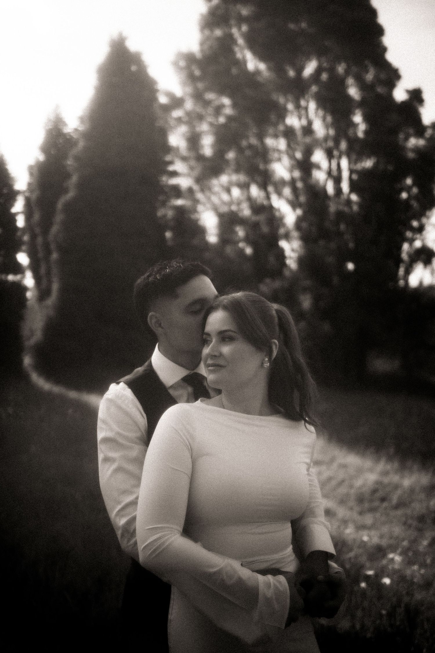 A romantic black and white photo series of a couple embracing in a misty forest setting at sunset.