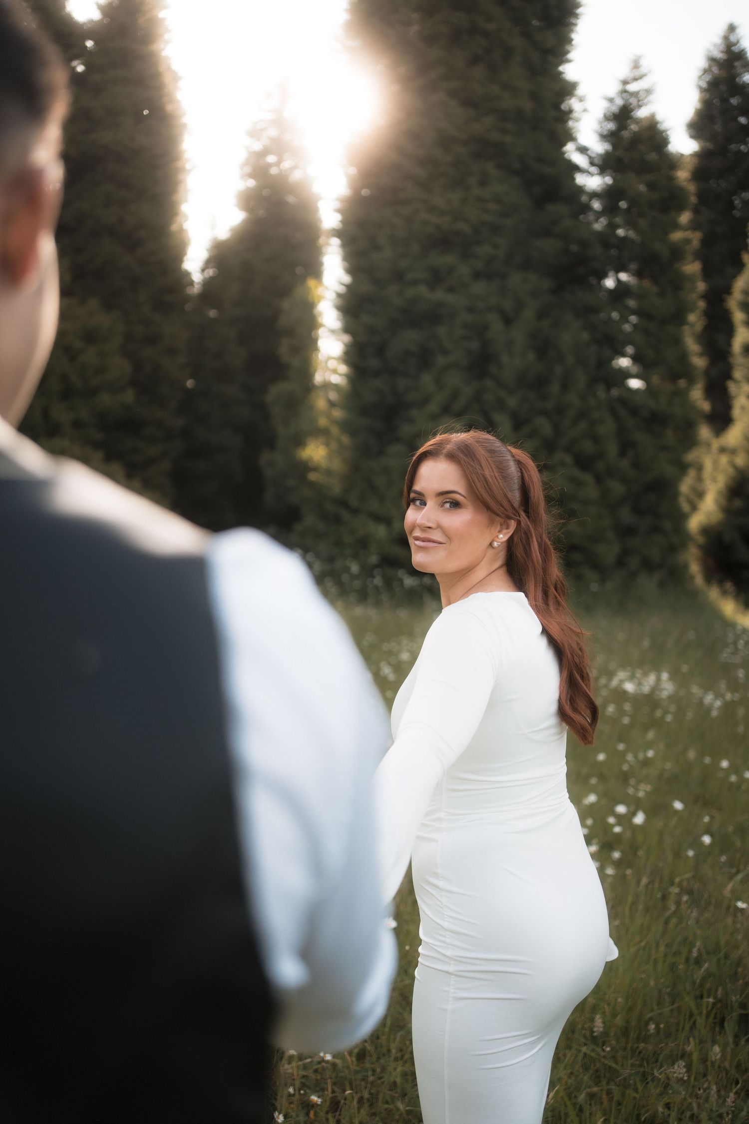 A couple in a field at sunset with evergreen trees in the background.