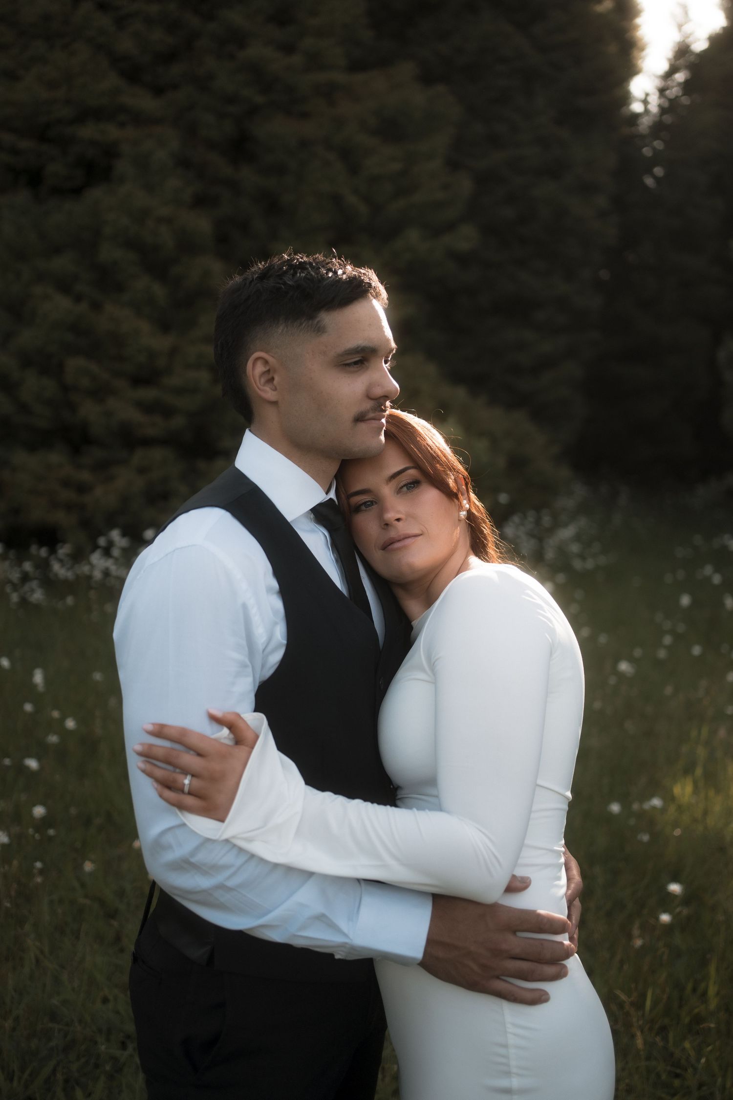 A romantic wedding couple embraces in a mountain meadow with evergreen trees in the background.