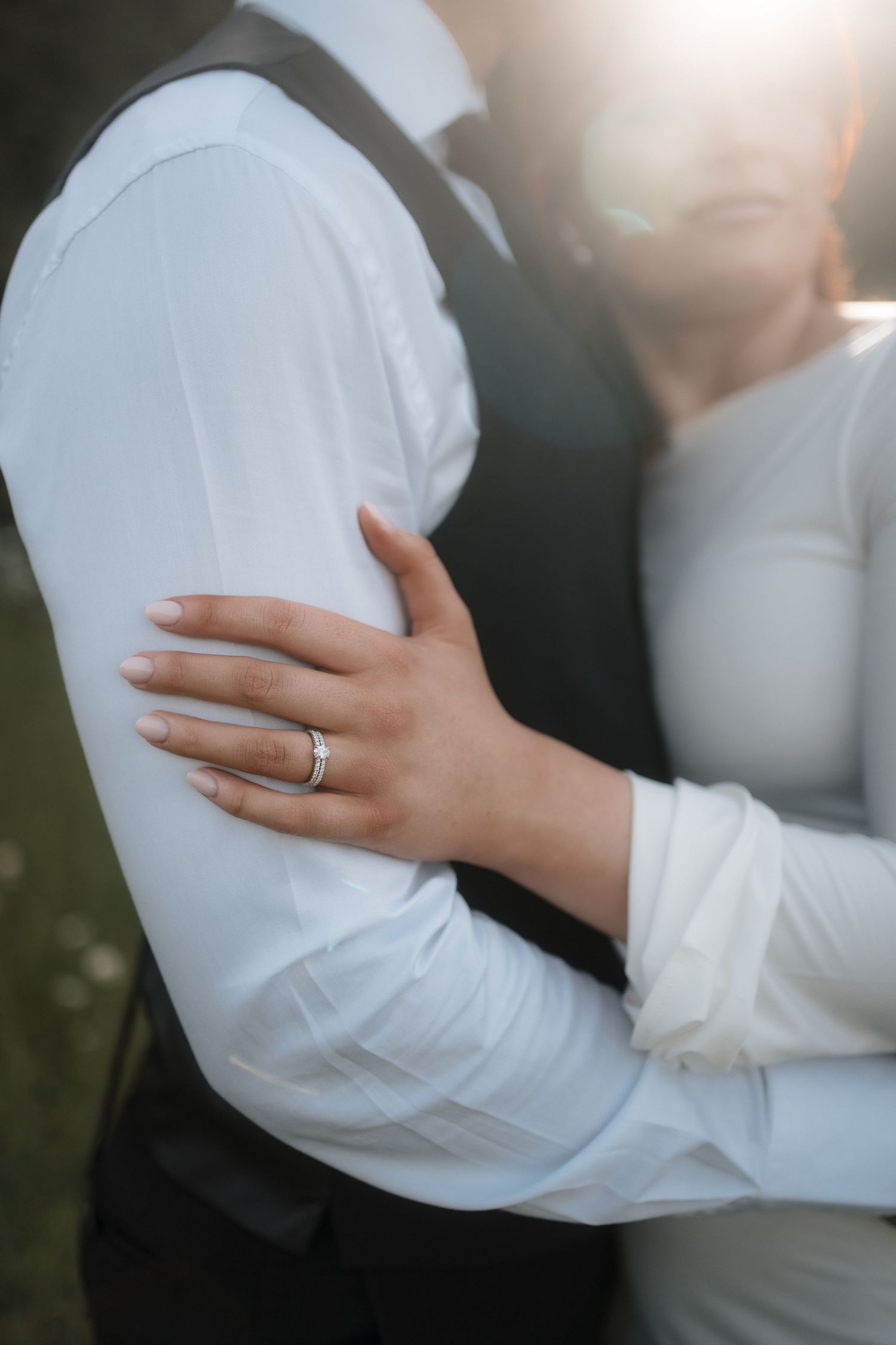 Intimate wedding portrait showing hands and white dress sleeves with a ring detail.