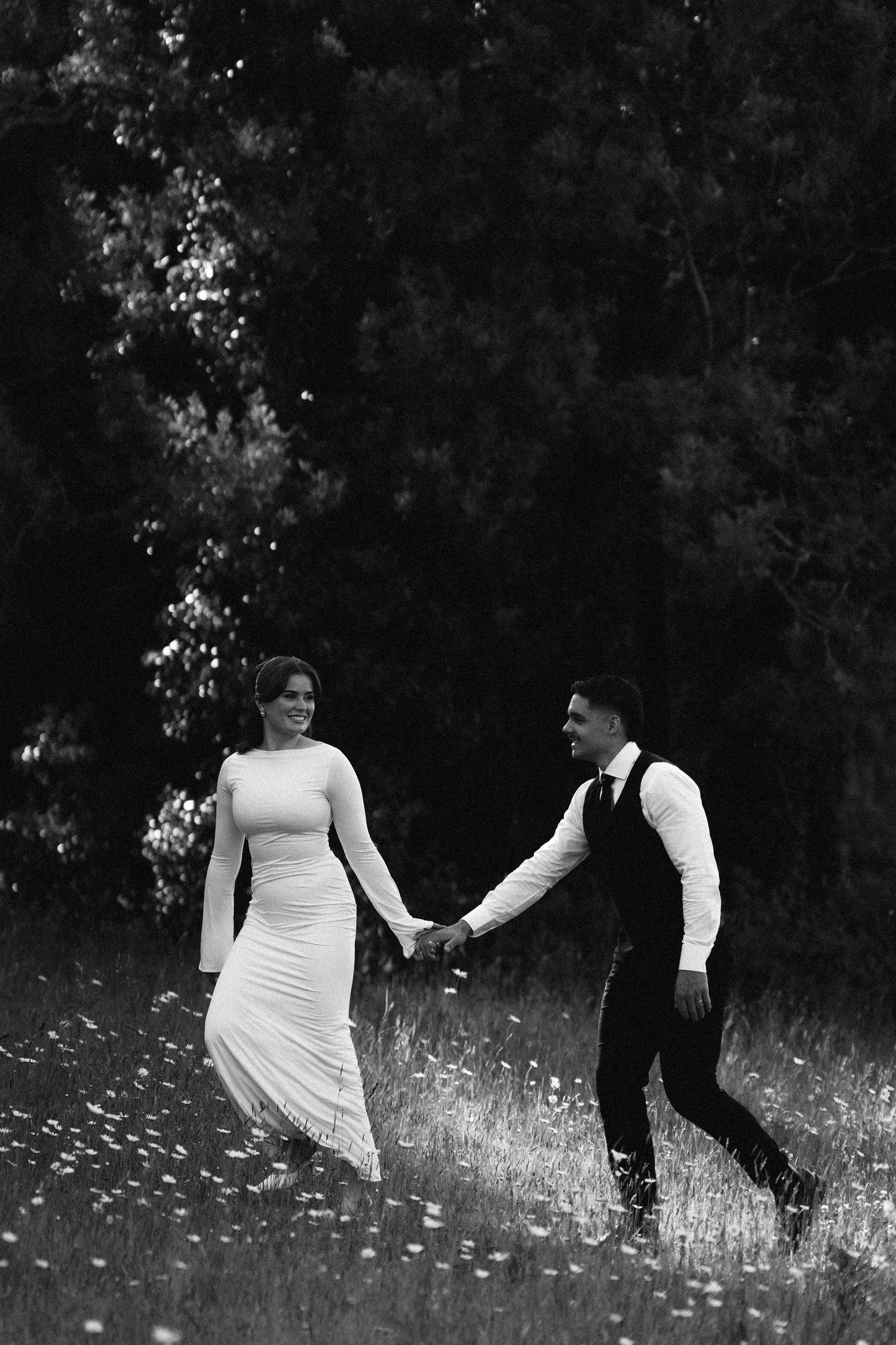 Black and white photo of a couple walking through a wildflower meadow.