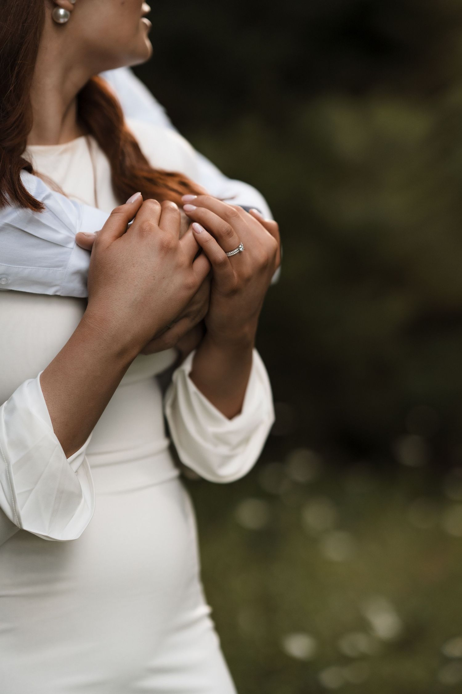 Close-up view of hands clasped together against a white sweater with a blurred natural background.