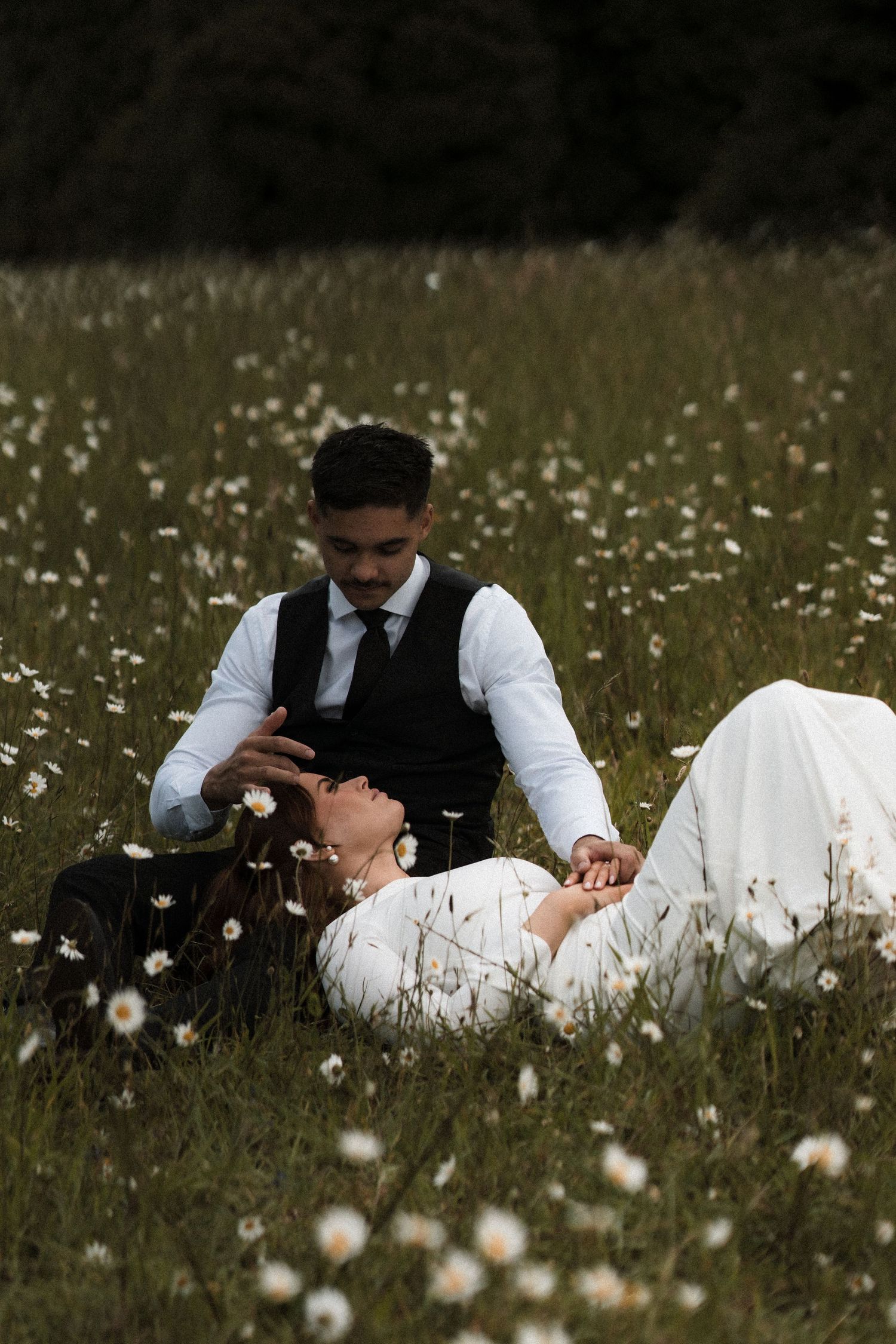 A couple in formal attire lies together in a wildflower meadow during a romantic photoshoot.