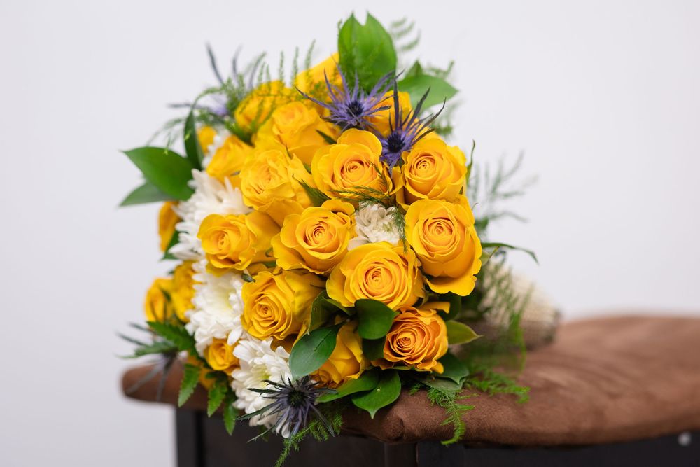 A bright yellow rose bouquet with white daisies and green foliage arranged against a light background.