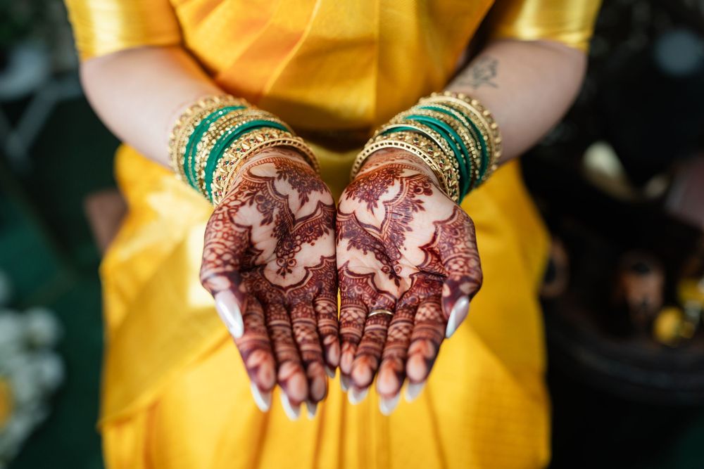 Hands decorated with intricate henna designs shown in a sequence against a yellow dress background.