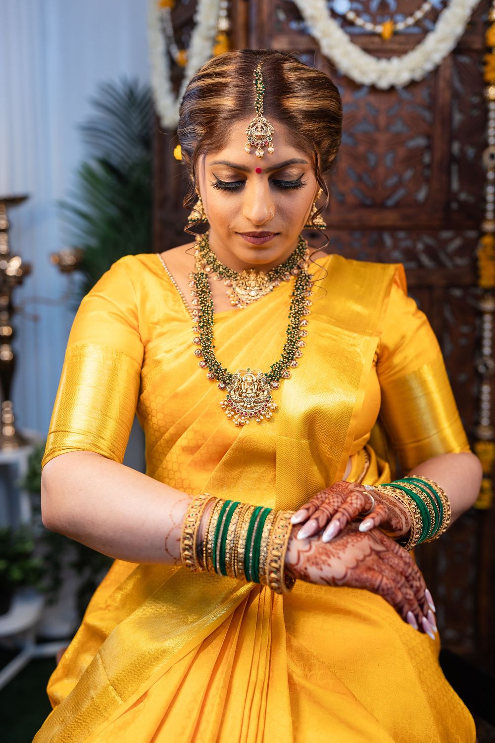 Traditional Indian bride in yellow silk sari adorned with jewelry and henna decorated hands.
