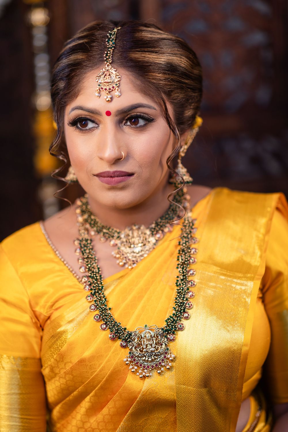 Traditional Indian bridal jewelry and makeup details with yellow silk saree and ornate gold necklace.