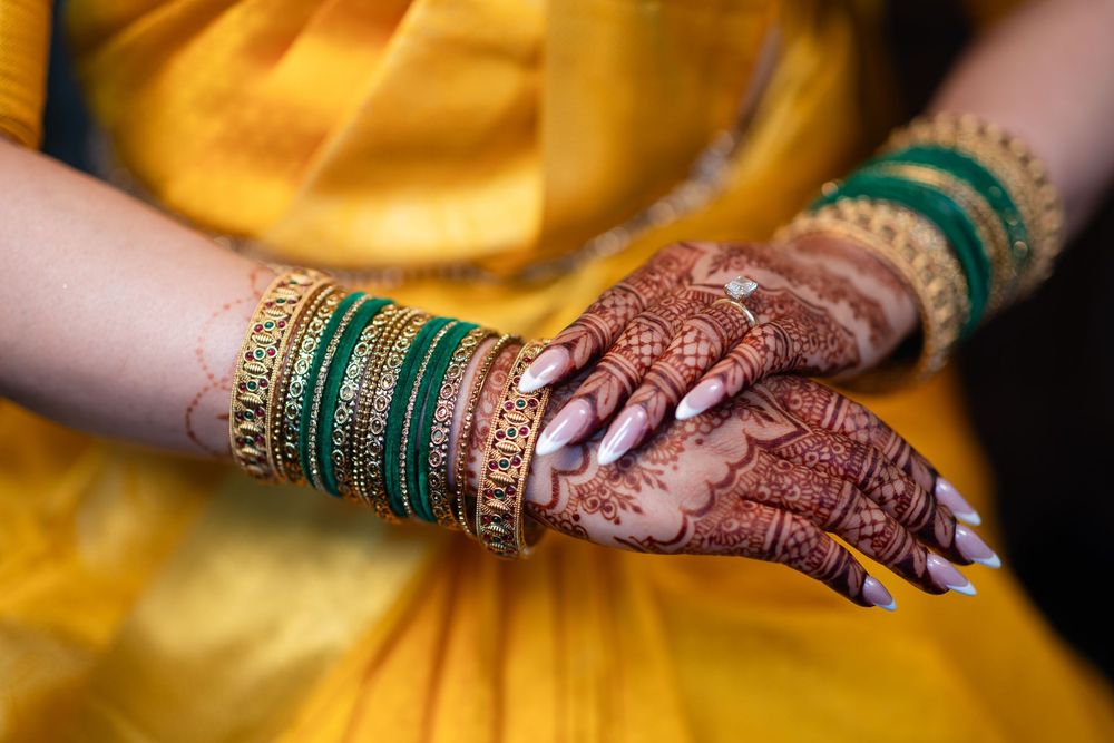 Detailed view of henna-adorned hands with green bangles against yellow fabric.