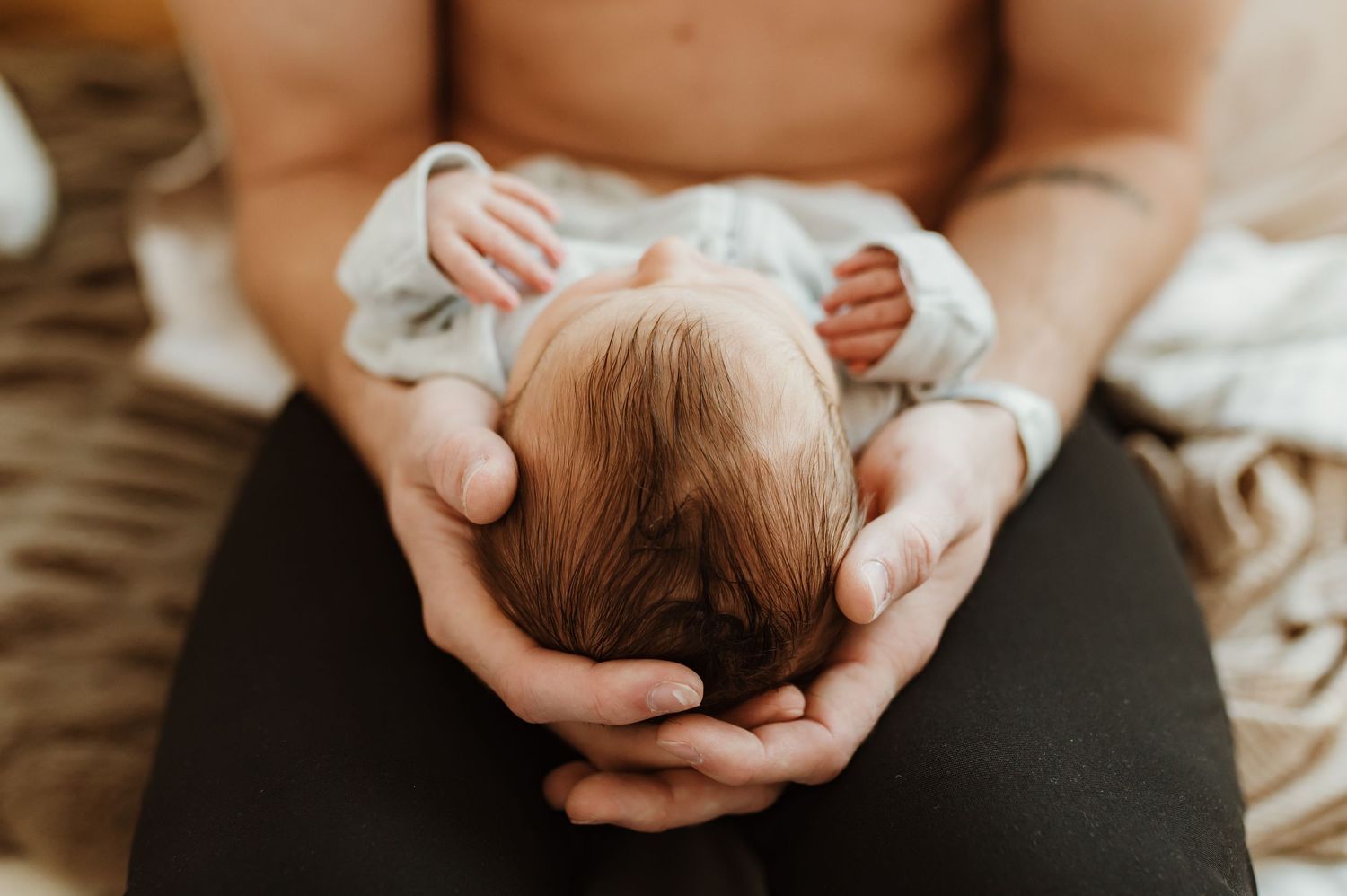 Hands gently cradle a newborn baby's head in a tender moment during a photoshoot.
