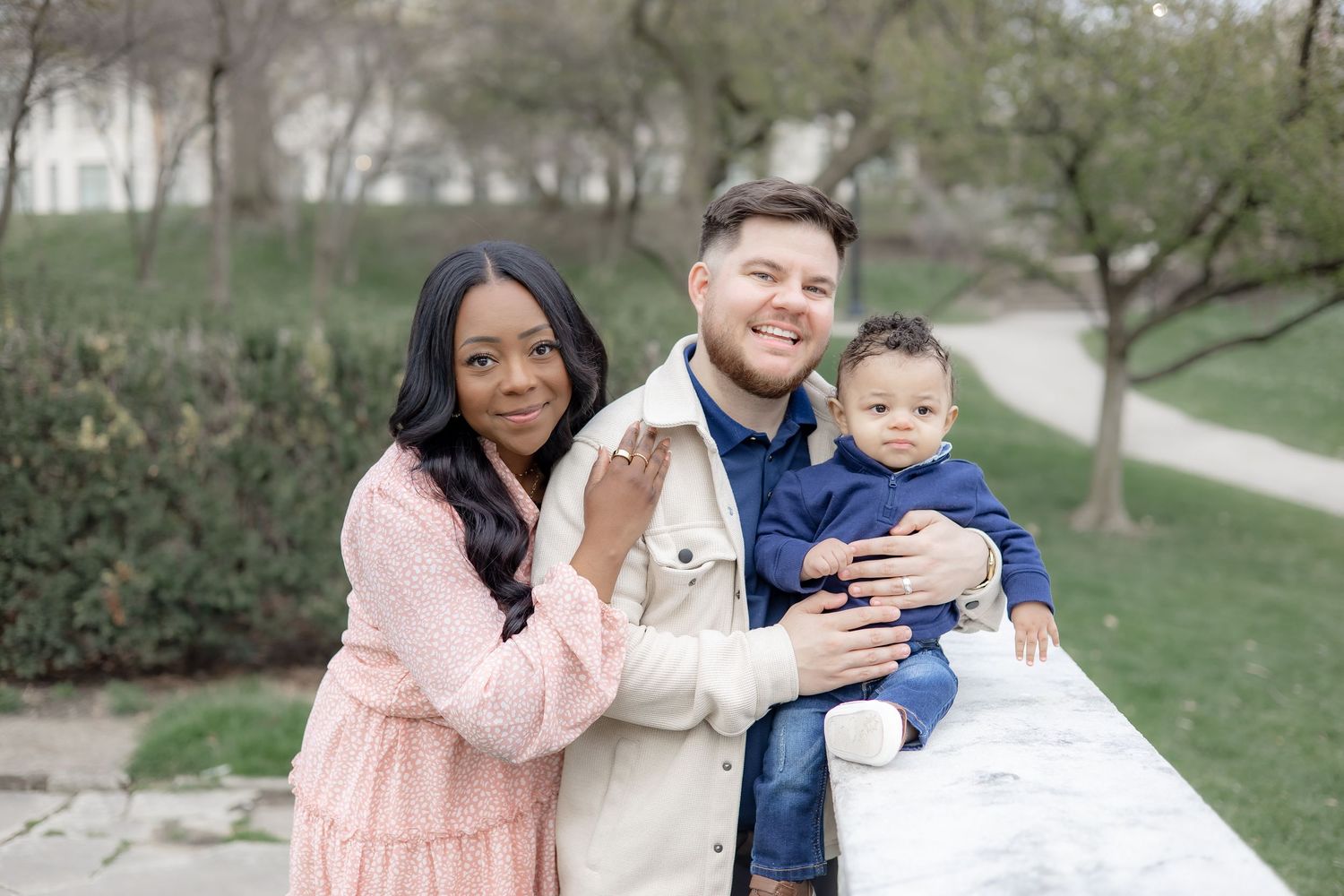 A family shares tender moments together outdoors during spring with cherry blossoms in the background.