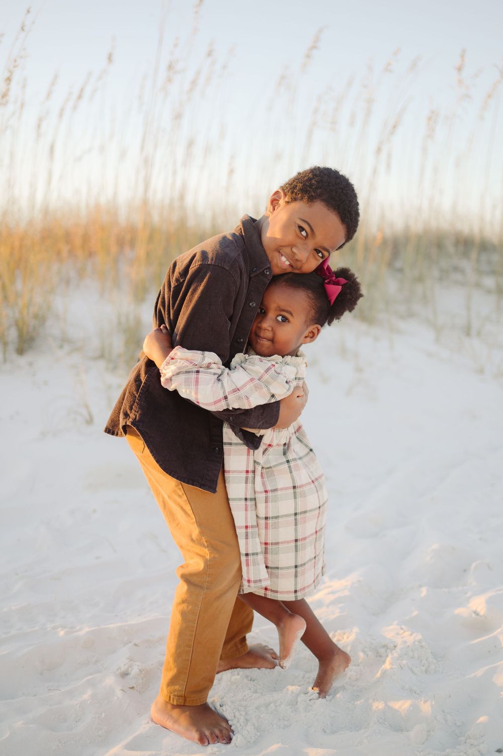 A parent and child share a playful moment together on a sandy beach with tall grass in the background.