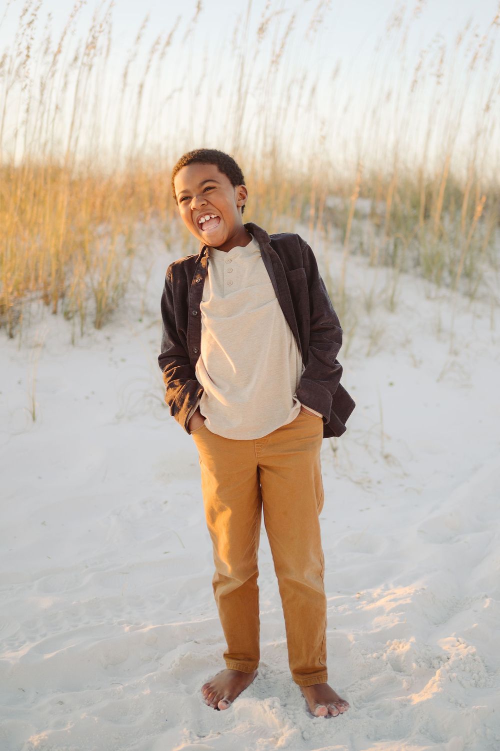 A child wearing khaki pants and a dark jacket plays on white sand dunes during golden hour.
