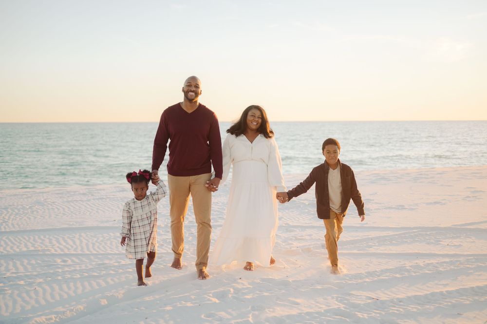Family walks together holding hands along a sandy beach at sunset with soft ocean waves in the background.