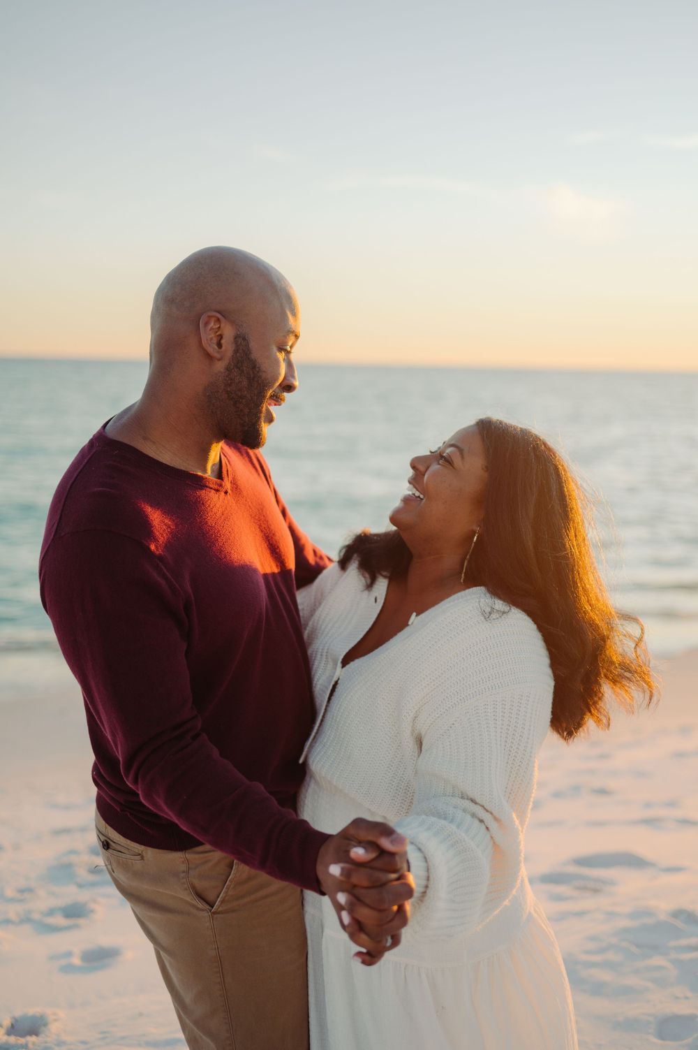 A romantic couple shares tender moments on a pristine beach at sunset with waves in the background.