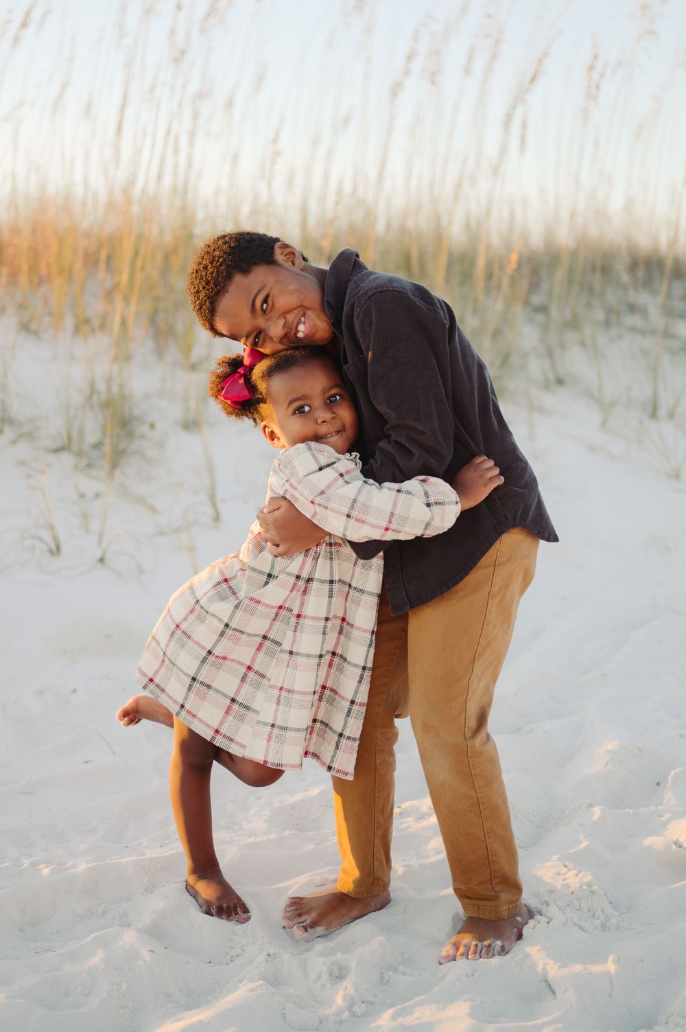A joyful embrace between two people on a sandy beach with tall grass in the background at sunset.
