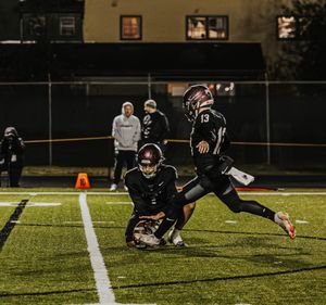 Football player diving to make a tackle during a night game on an illuminated field with other players in motion.