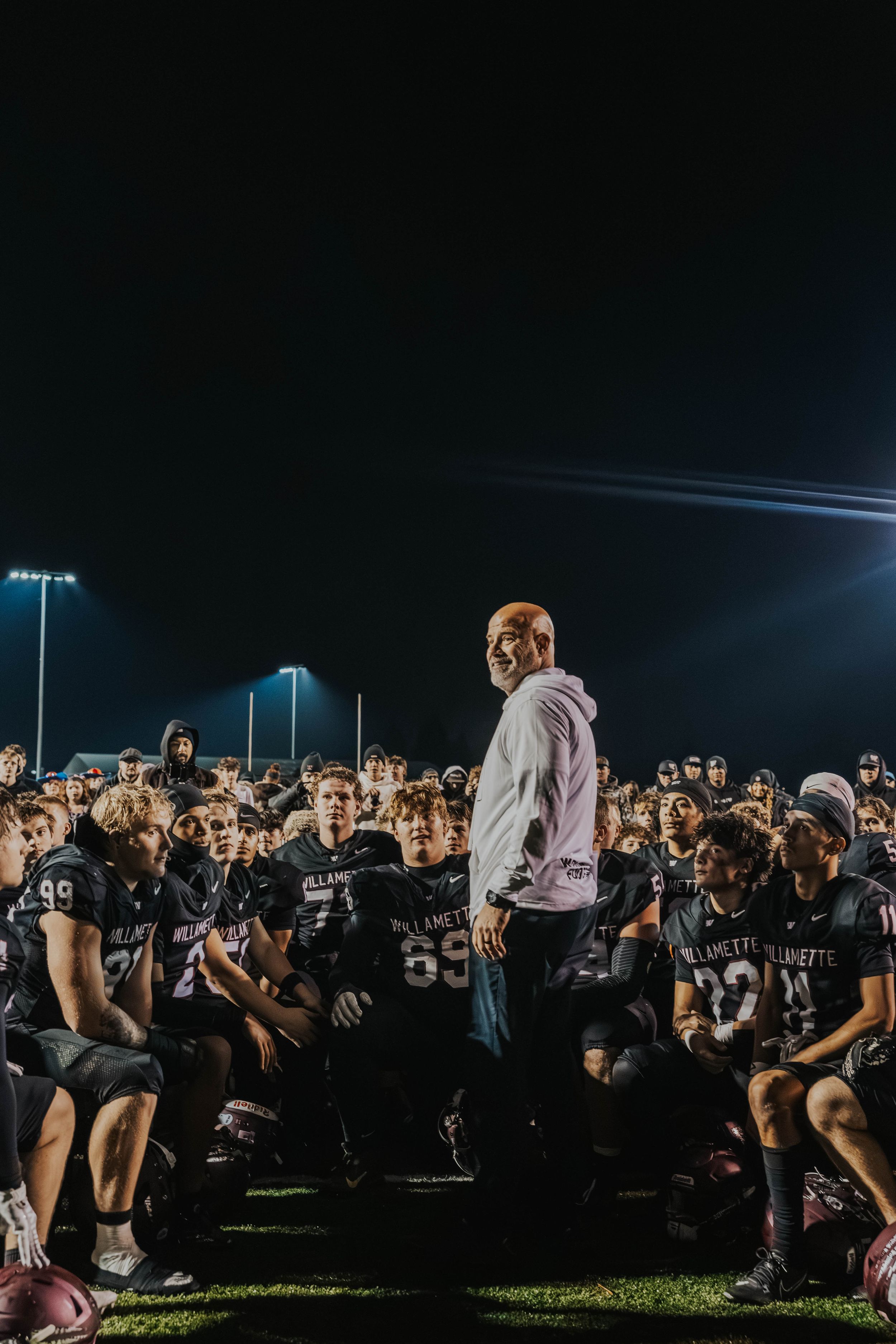 Football players and fans celebrate on a dark field after a game under stadium lights.