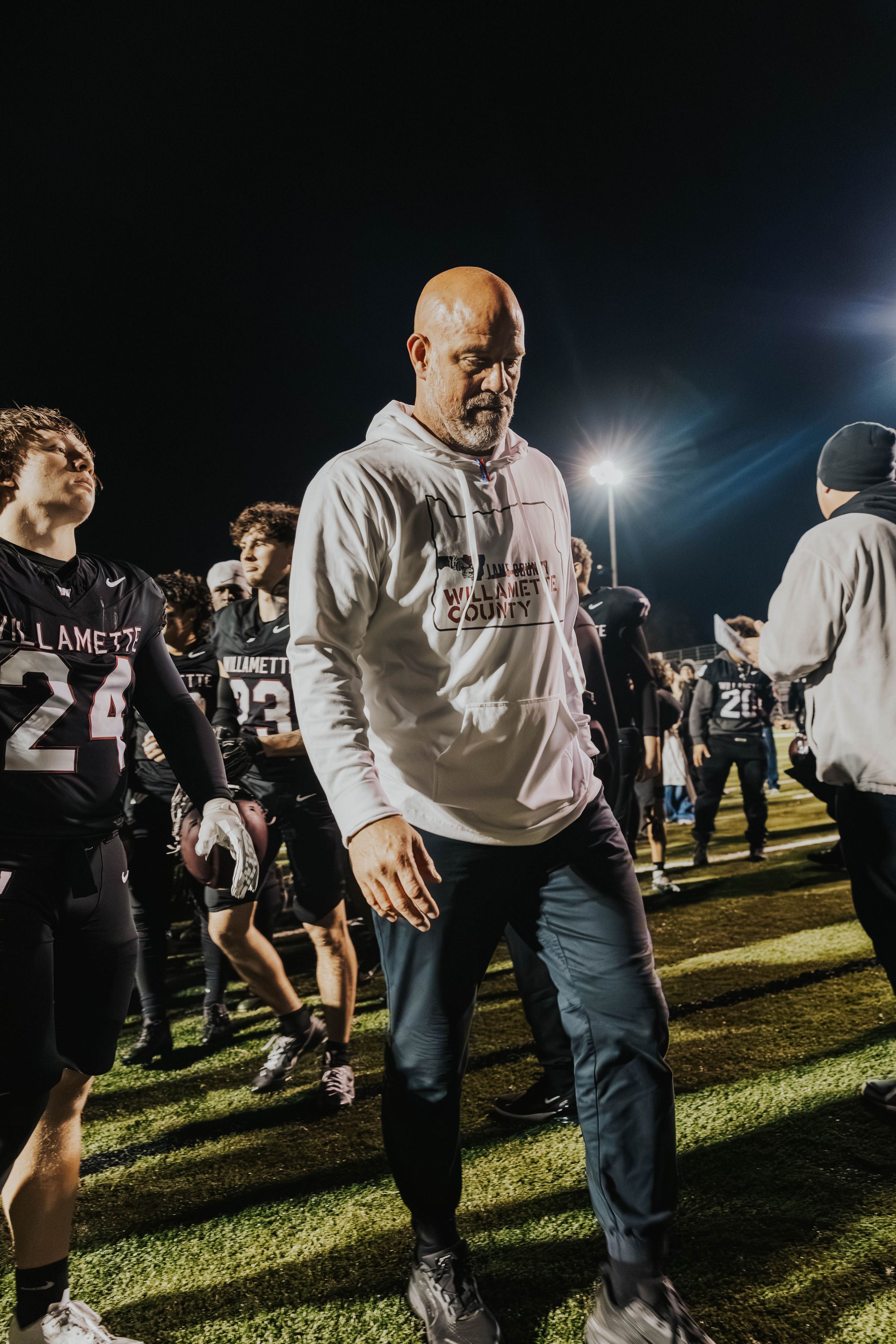 Football team members gather on a nighttime field under bright stadium lights during practice or game preparation.