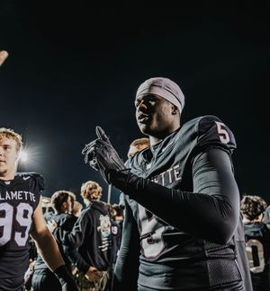 Football players gather on a dark field during a nighttime game wearing black uniforms and helmets.