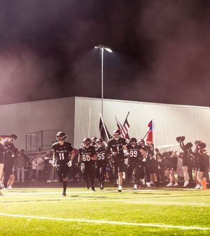 Football players kneel on a foggy field at night during a dramatic pre-game ceremony with stadium lights glowing.