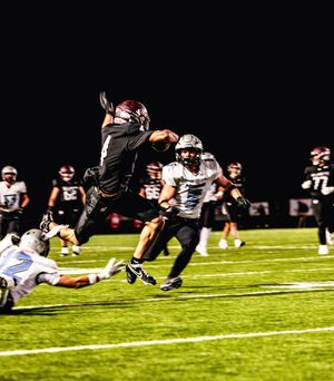 Football player leaps high into the air to avoid a tackle during a nighttime game on an illuminated field.