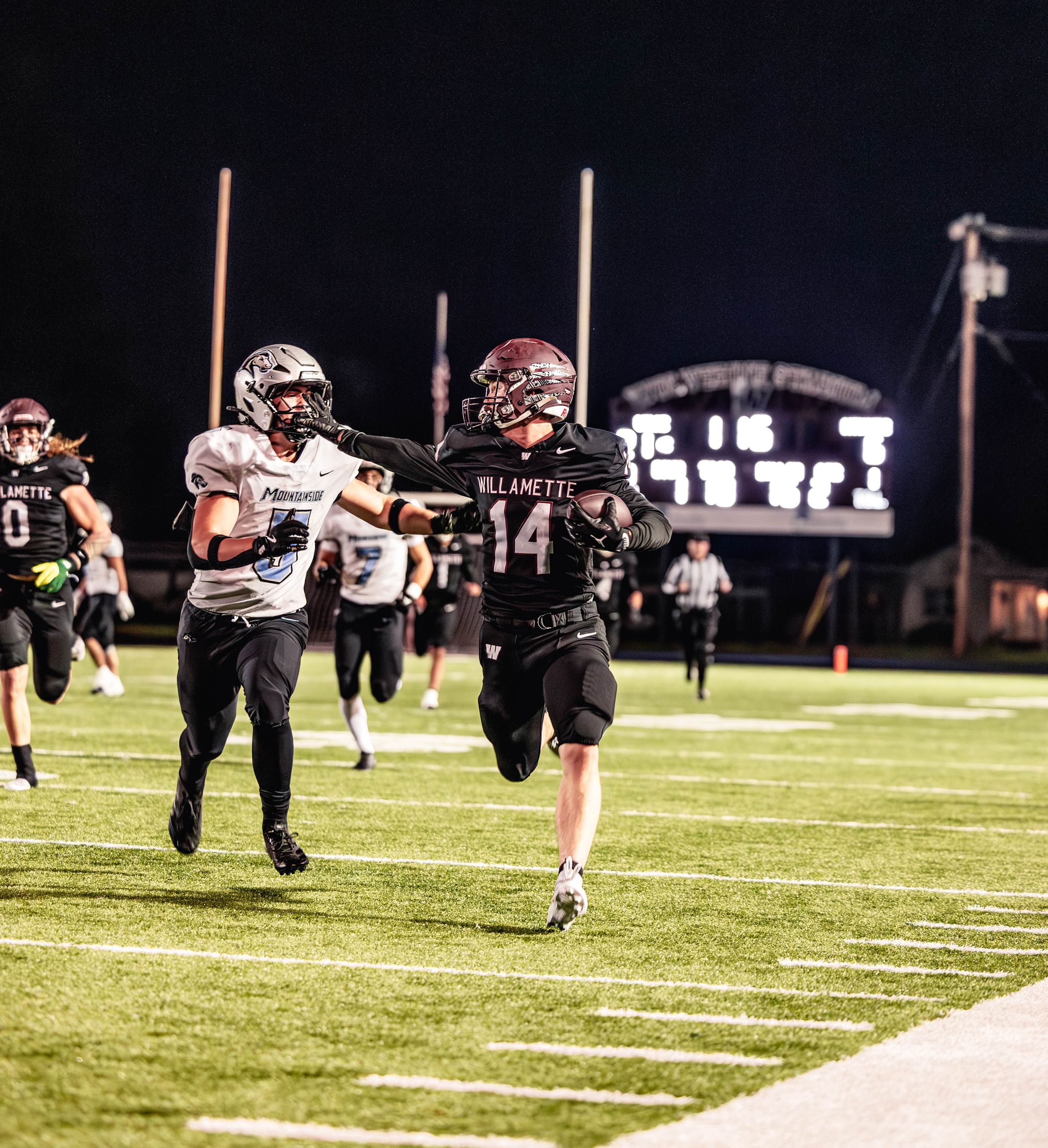 Football players dive and stretch during a nighttime practice session on an illuminated field.