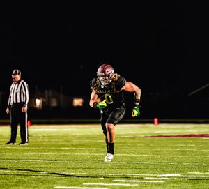 Football player in black uniform kicks the ball during a nighttime game on an illuminated field.