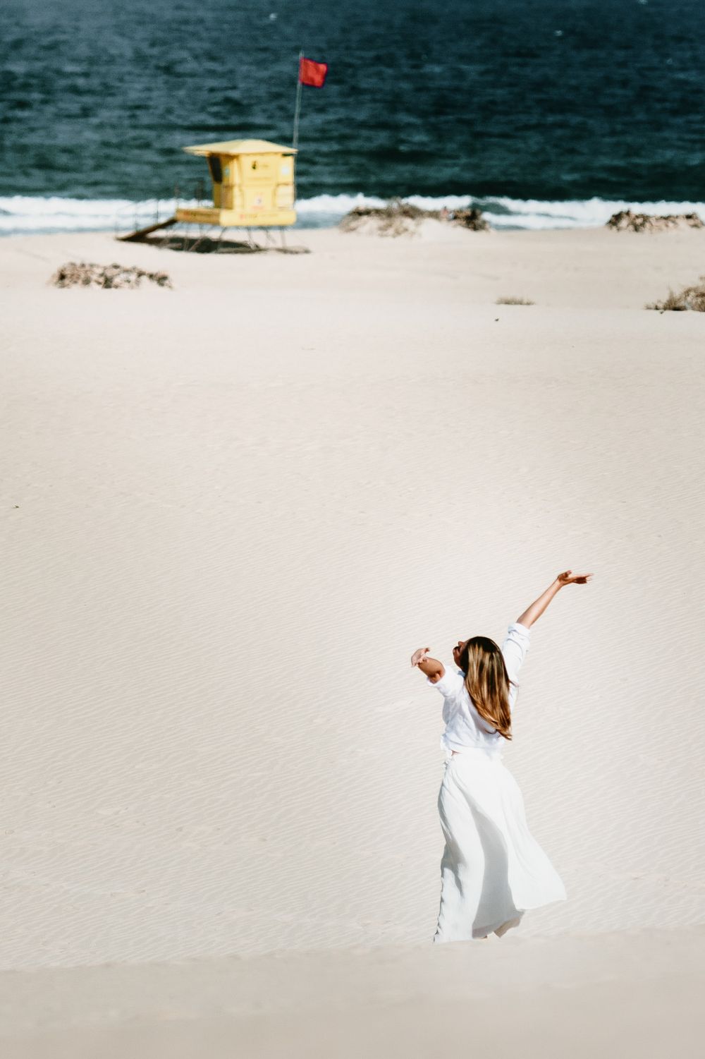 Woman in a white dress celebrating with arms open in the dunes - Freedom and travel portraits by photoFuerte
