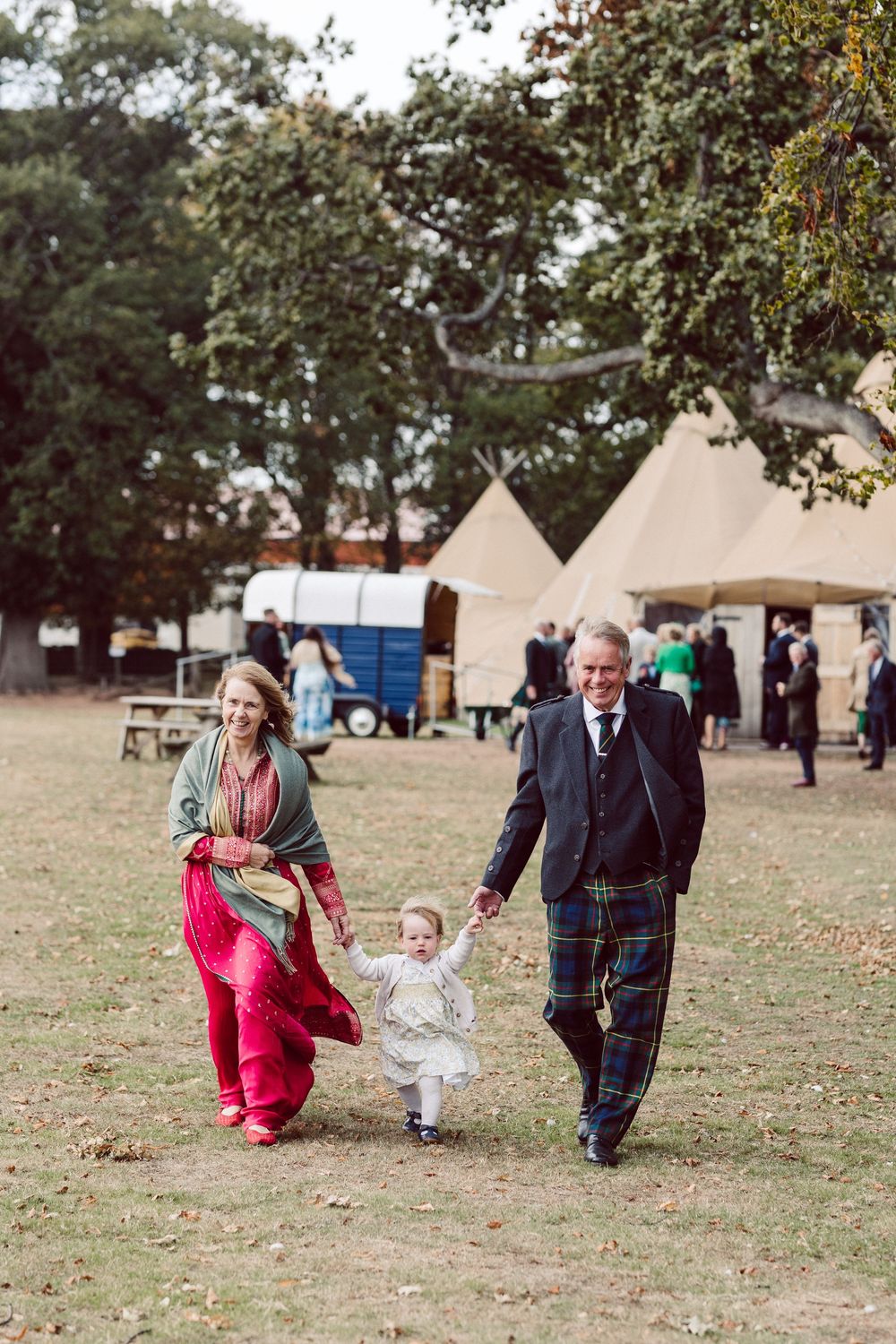A sequence of candid outdoor shots shows a small child learning to walk with adults in a grassy field.