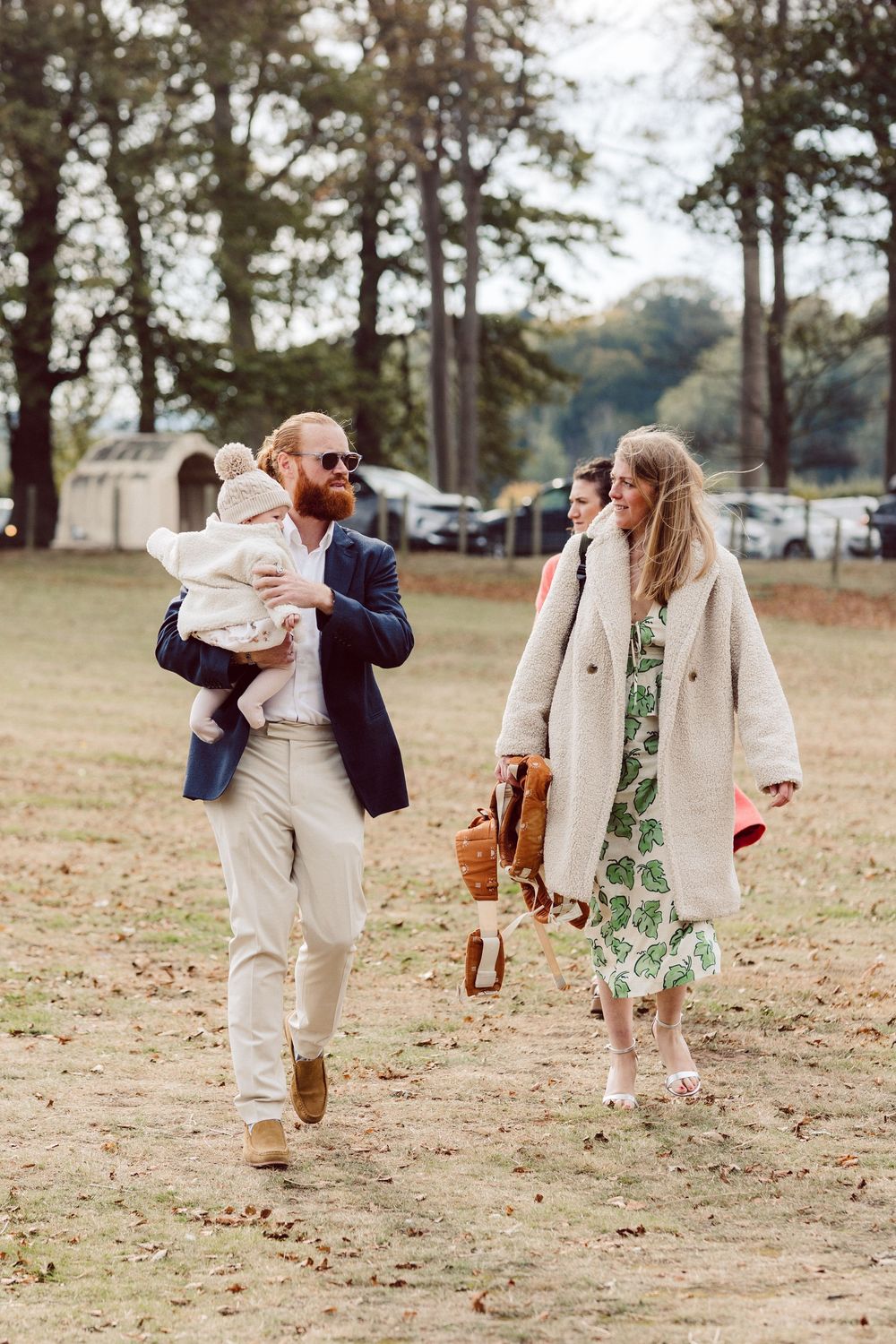 A couple in coordinated outfits playfully runs and dances together across a grassy field on an autumn day.