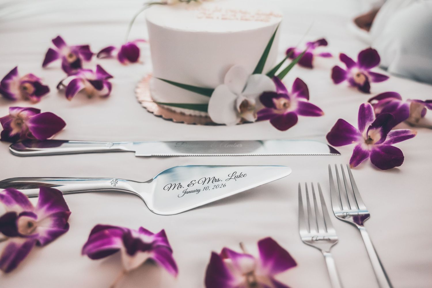 Elegant place setting with purple orchids, white plates, and silver cutlery on a light colored surface.
