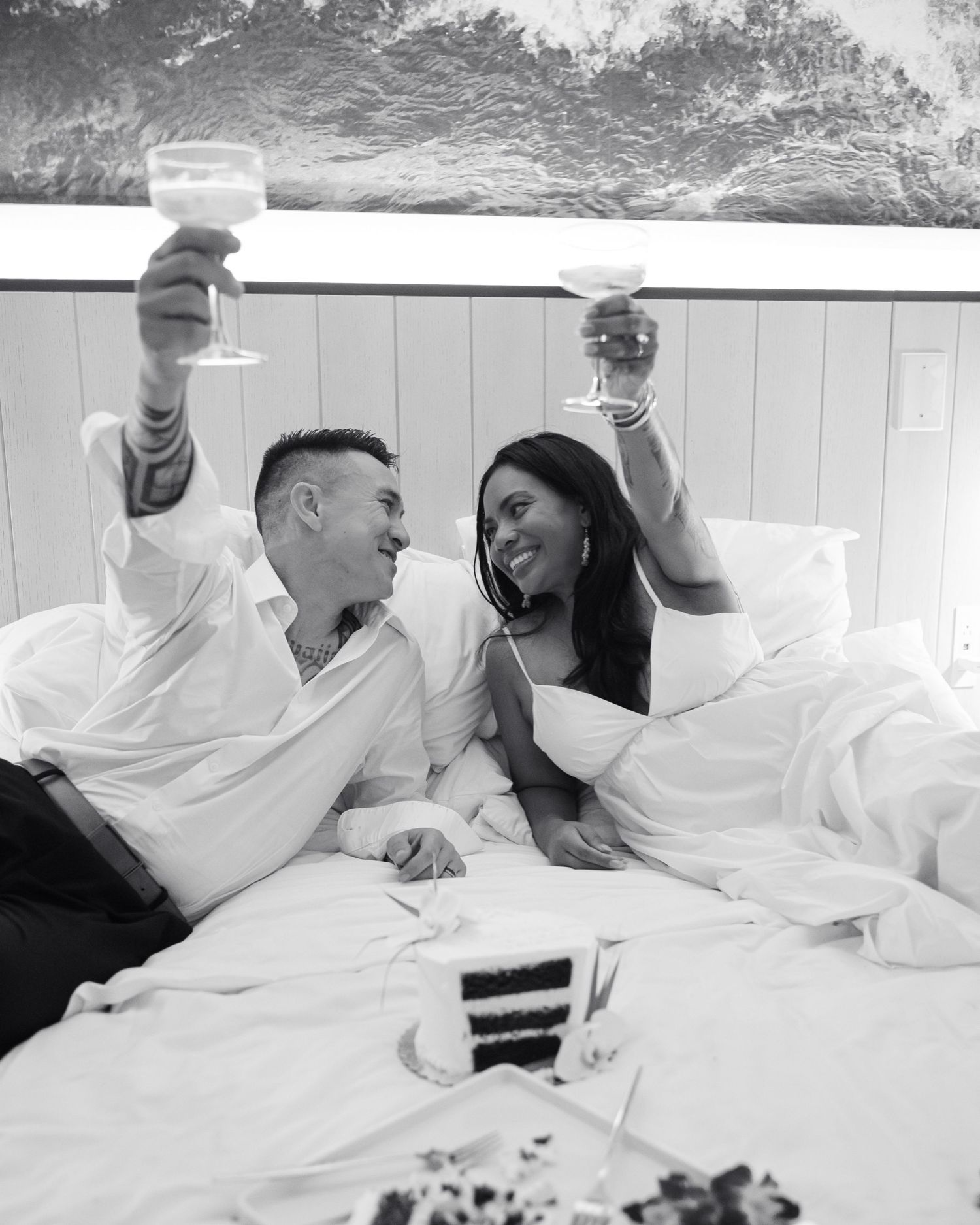 A couple shares intimate moments together while relaxing in white bedding during a casual lifestyle photoshoot.