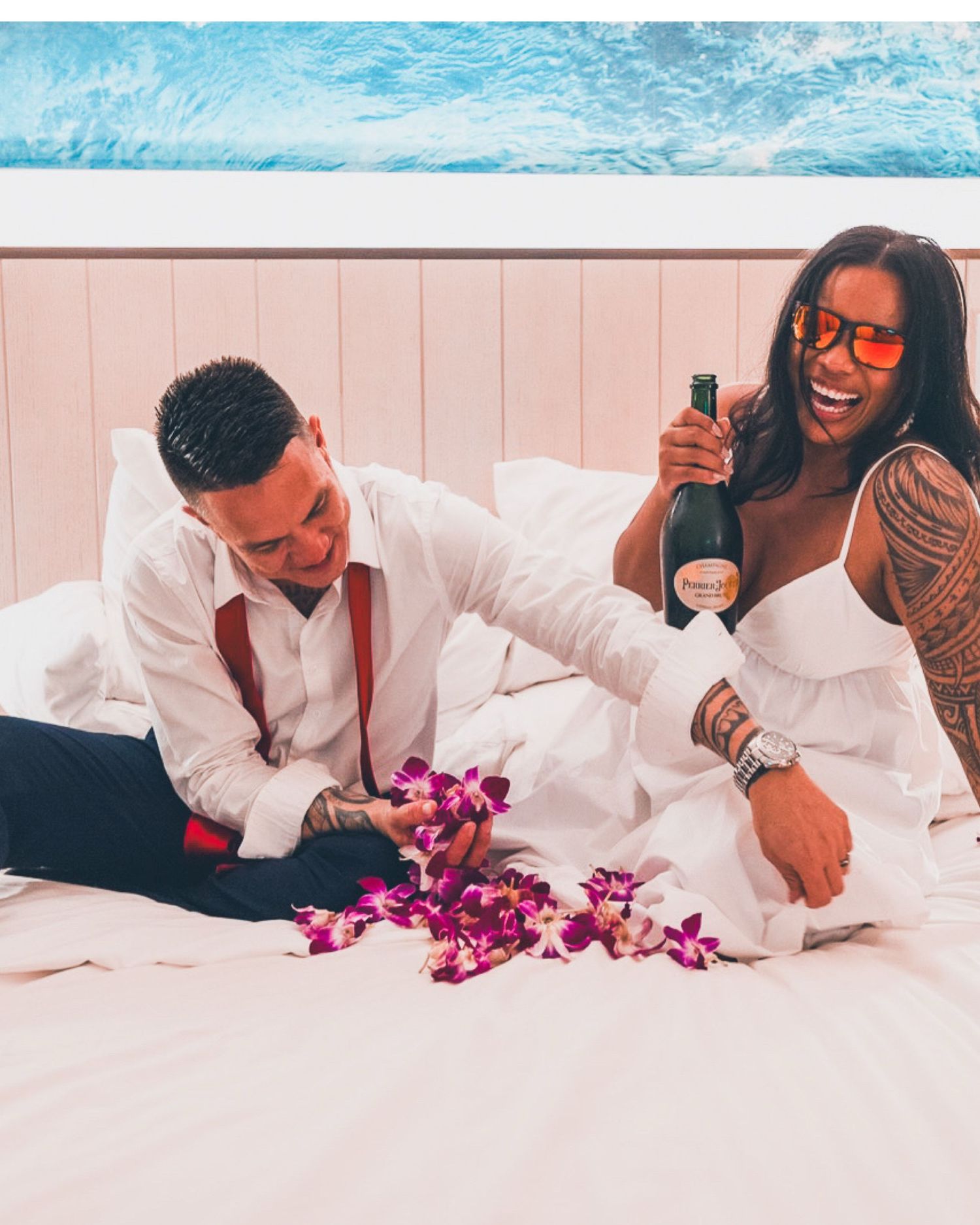 A couple lying on white bedding with purple orchids creating a romantic atmosphere.