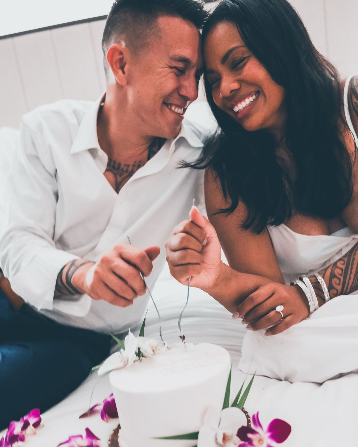 Intimate couple sharing tender moments together on white sheets with orchid flowers.