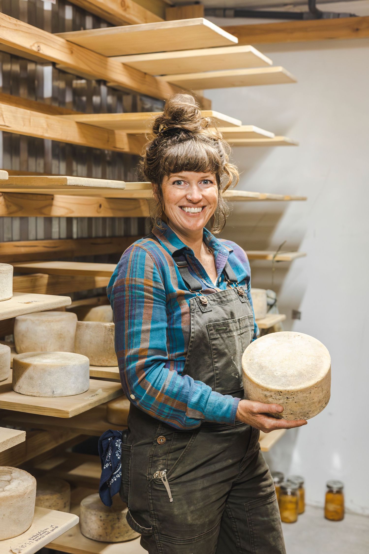 Artisanal cheese aging on wooden shelves in a cellar while someone tends to the rounds.