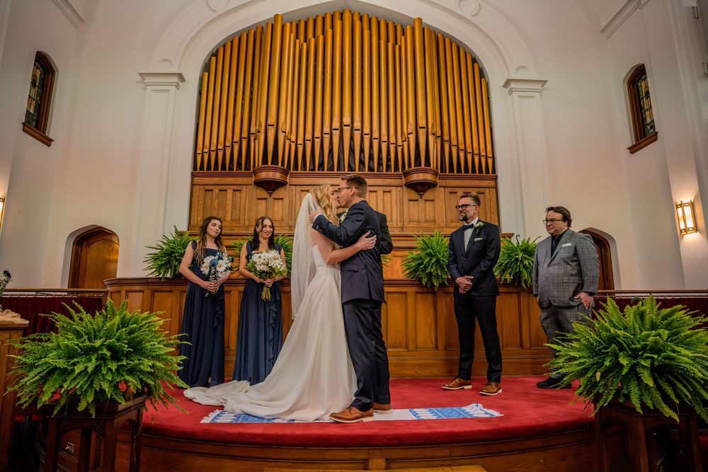 Wedding ceremony taking place in a traditional church sanctuary with wooden organ pipes and green plants as decor.