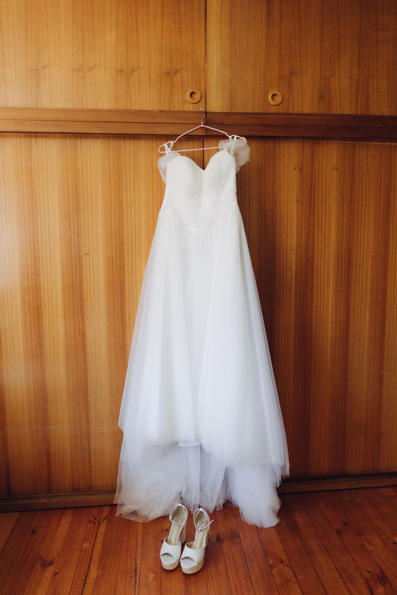 Elegant strapless white ball gown wedding dress hanging with bridal heels below.