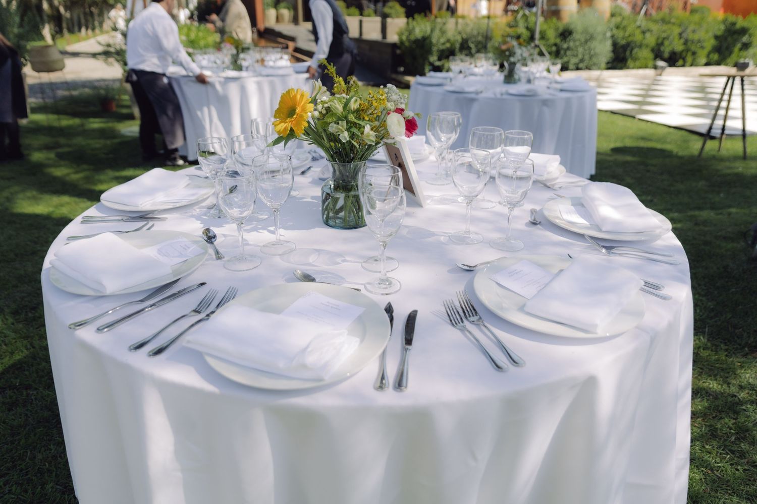 Elegant outdoor wedding reception table set with white linens and sunflower centerpiece.