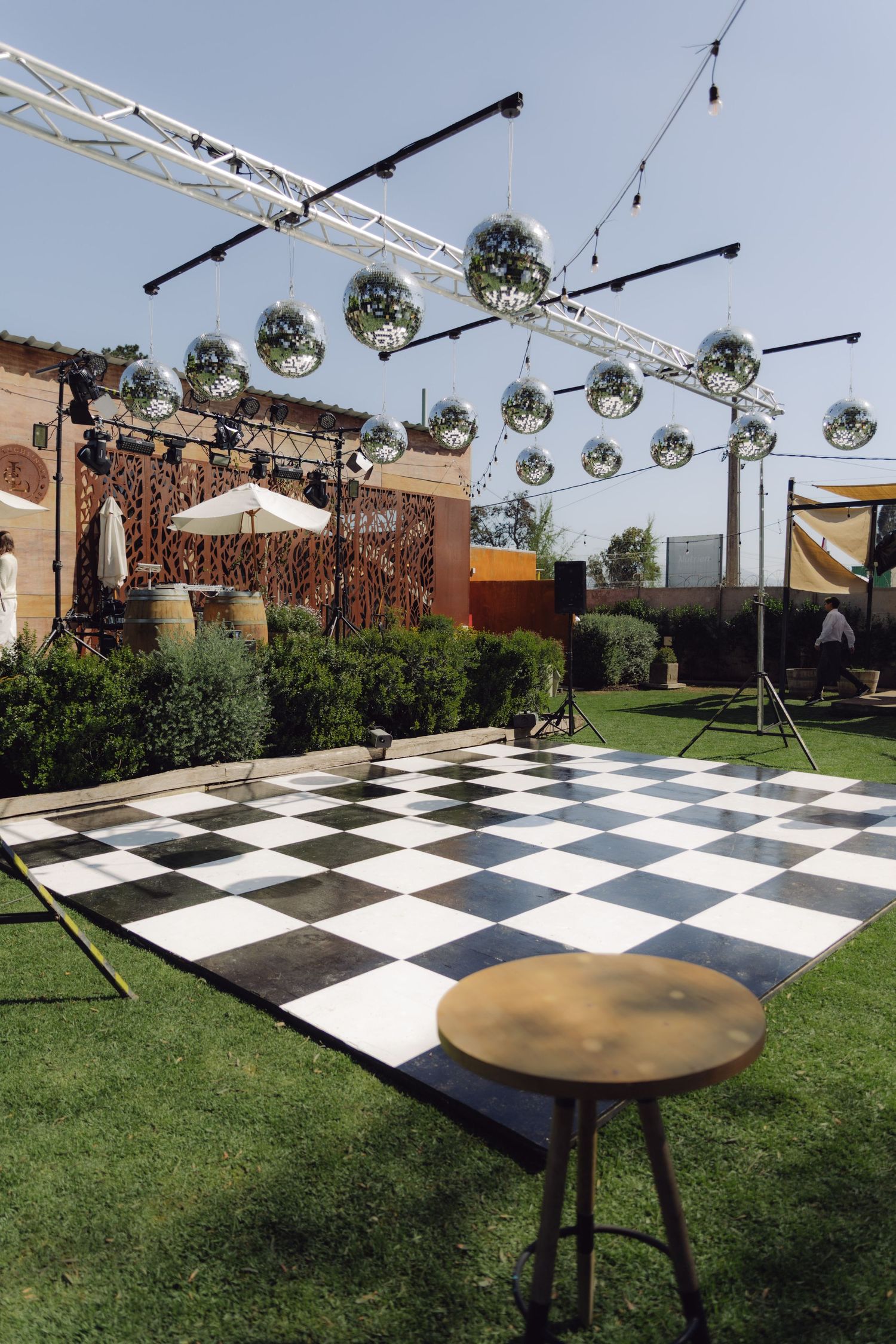 Outdoor wedding dance floor with black and white checkered pattern, disco balls overhead, and green lawn setting.