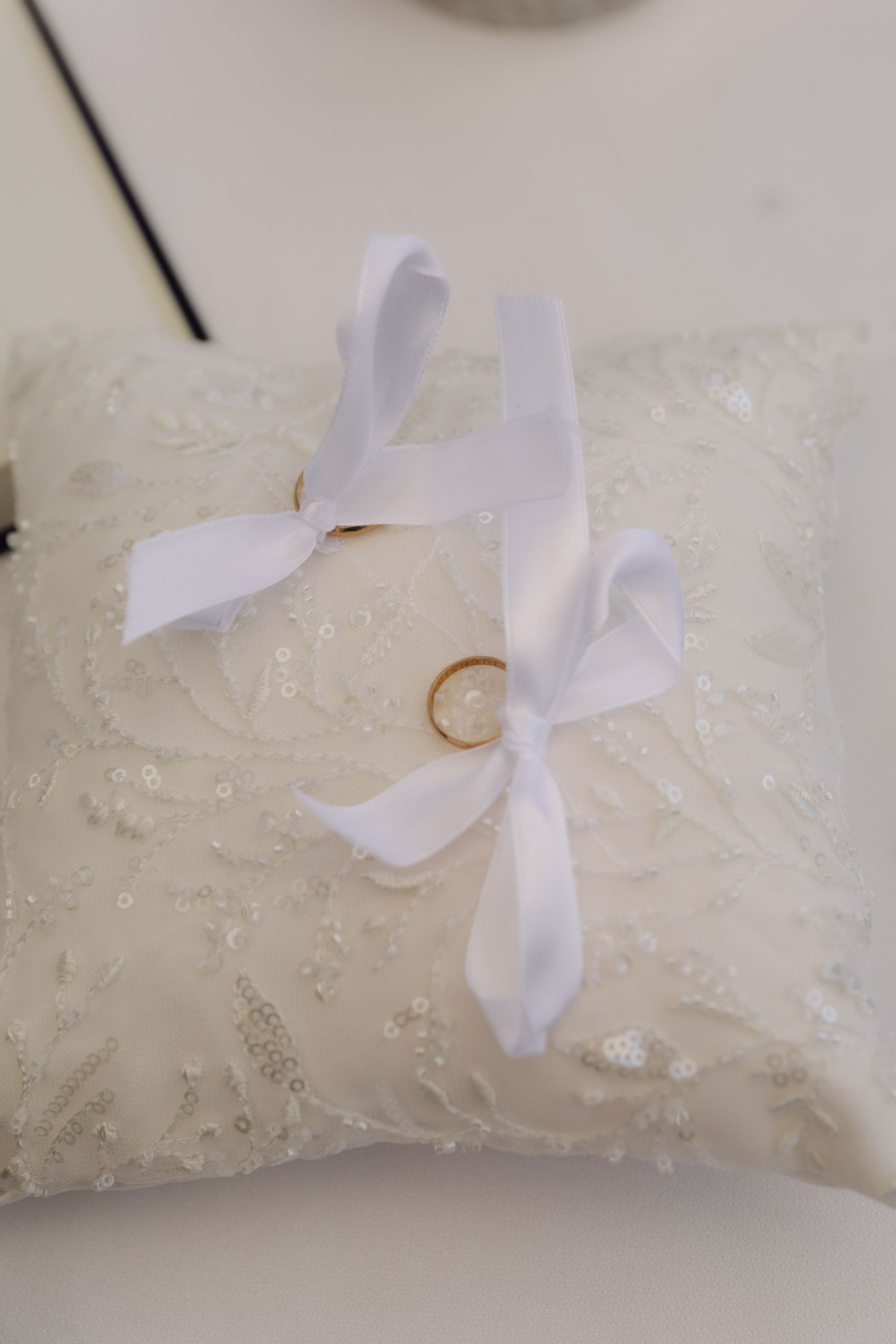 Two gold wedding bands displayed on white lace ring bearer pillow with satin ribbon bows.